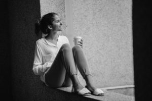young adult woman sitting down drinking coffee bw
